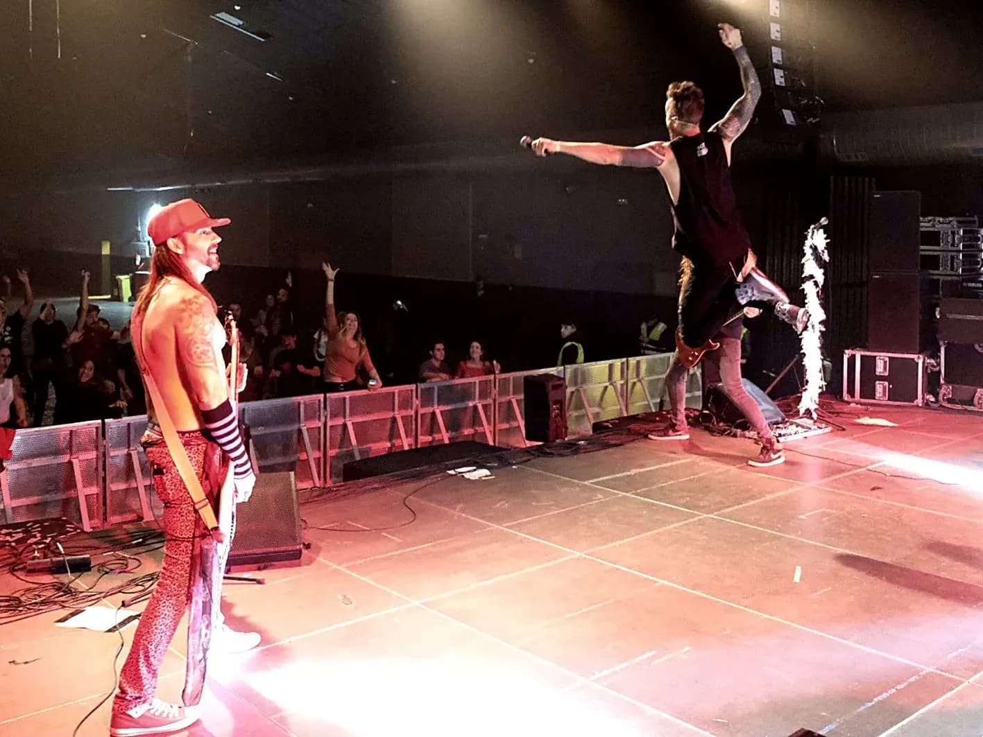 Vocalistas de Big Mouthers saltando sobre escenario, uno con gorra roja y torso pintado y otro con brazo levantado