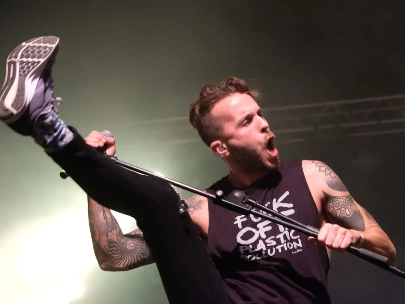 Vocalista de Big Mouthers cantando con pierna levantada y camiseta negra mostrando tatuajes en el escenario