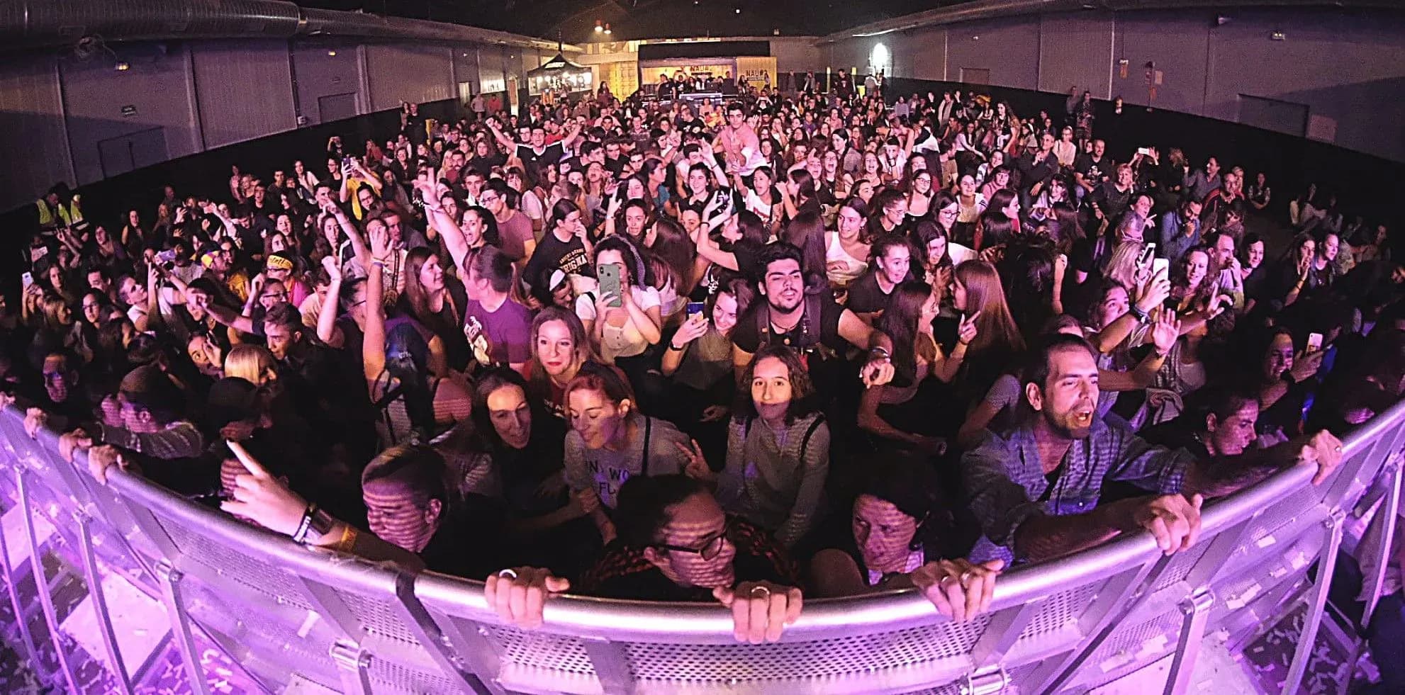Publico abarrotado con manos en alto frente a la cabina de DJ en discomovil con iluminacion rosa