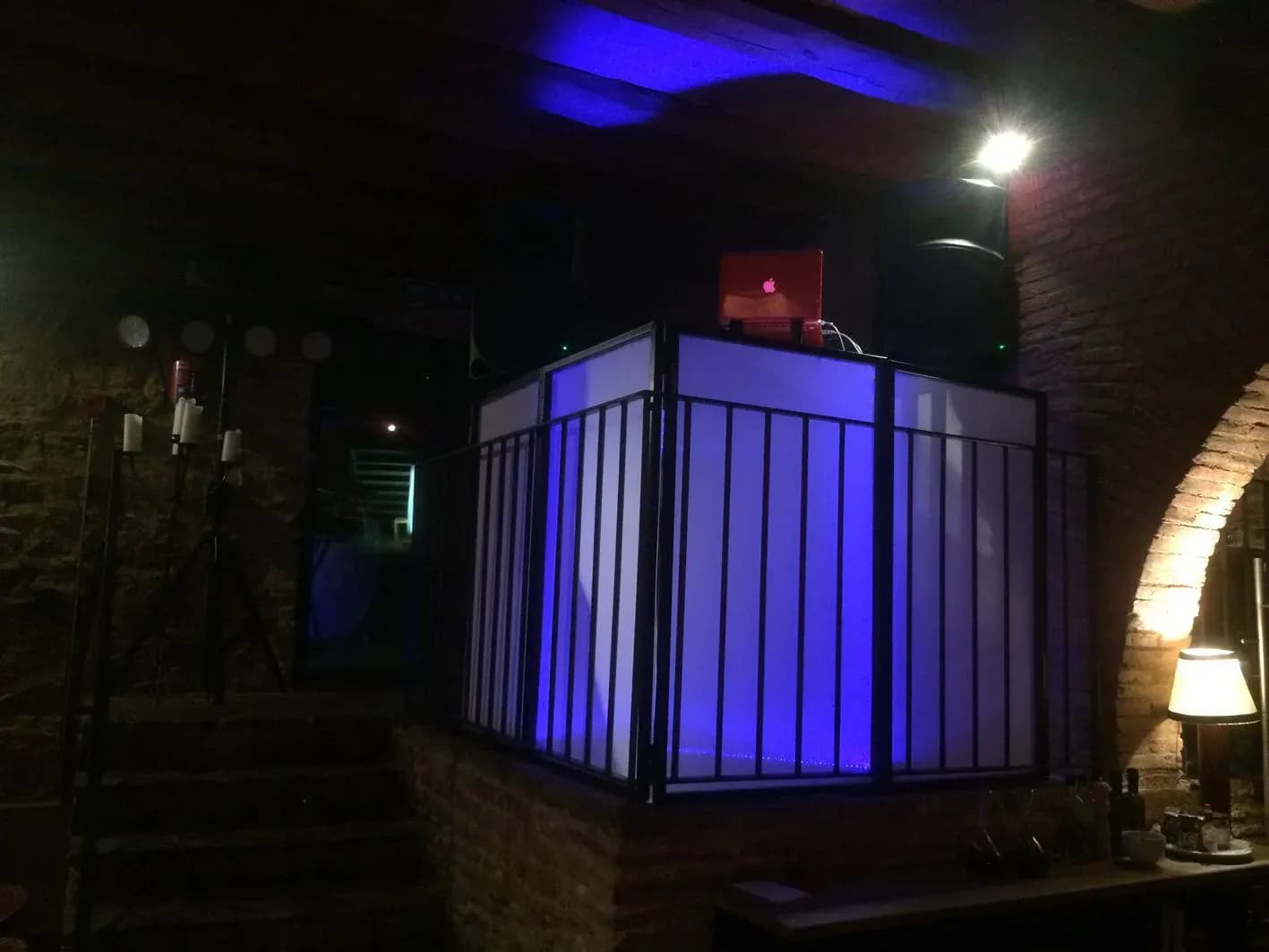 Cabina de discomovil con pantallas blancas iluminadas en azul, altavoz y portatil rojo en sala con bovedas de ladrillo