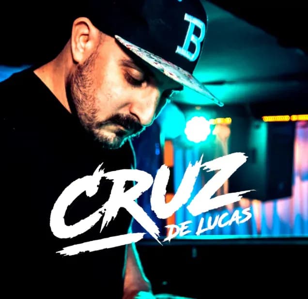 DJ Cruz de Lucas con gorra y barba inclinado sobre la mesa de mezclas con luces azules