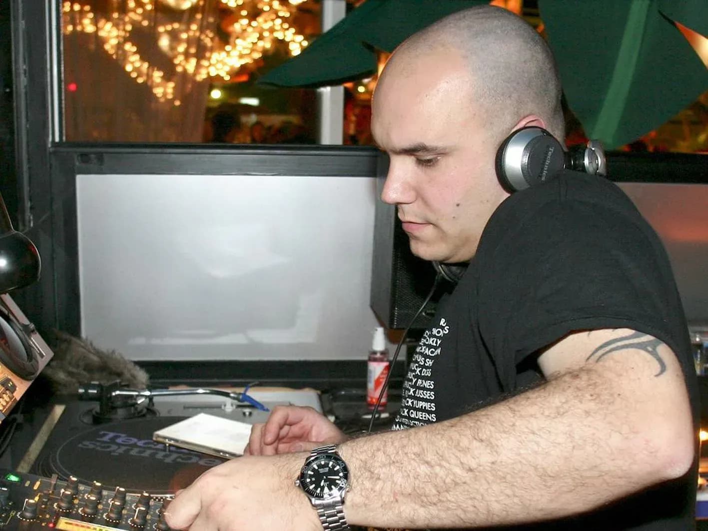 DJ Jordi joven con tatuaje tribal en el brazo manipulando plato Technics con auriculares plateados en sala vintage