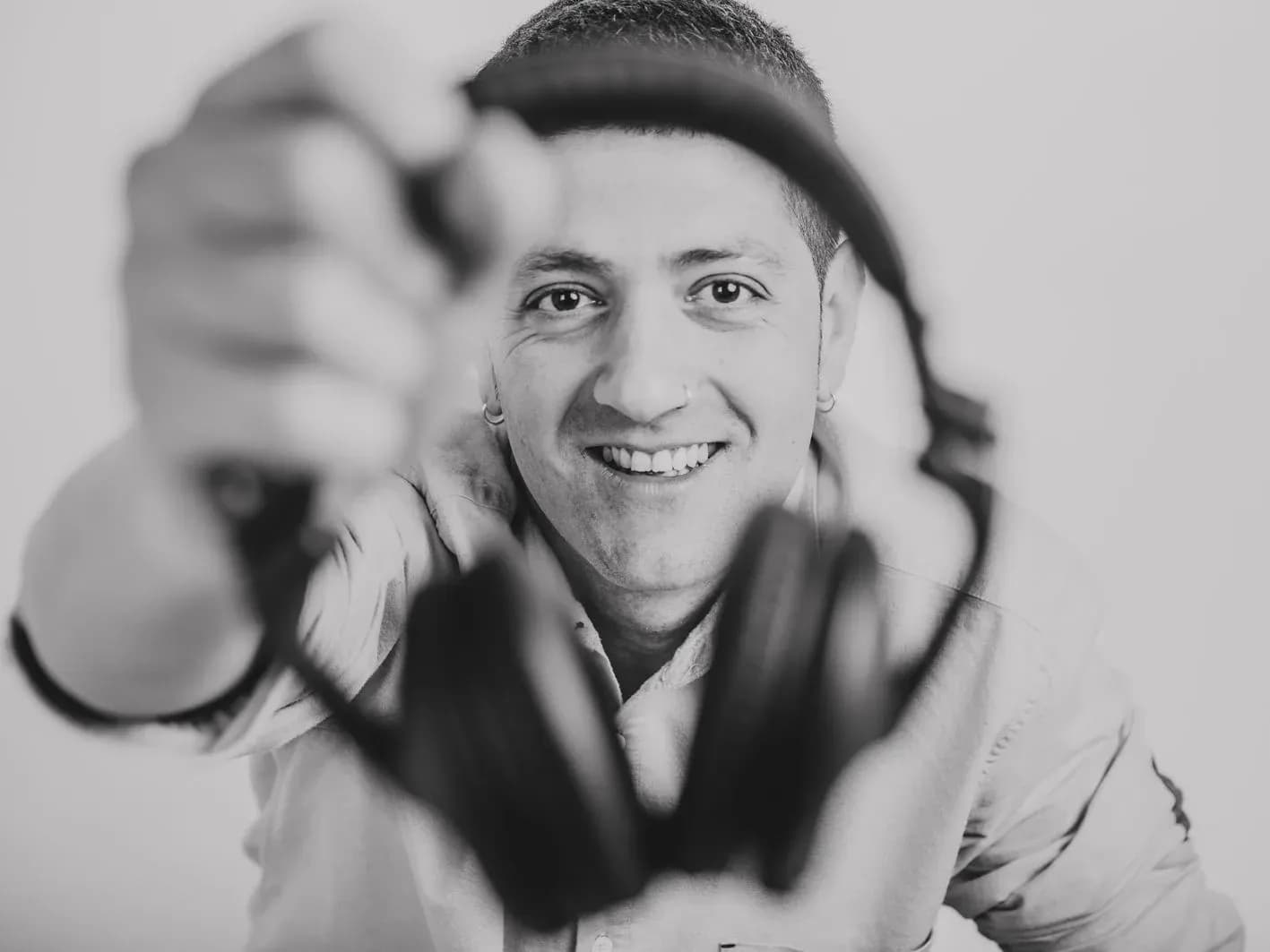 Pablo Picón sonriente ofreciendo unos auriculares a cámara en plano cercano, retrato en blanco y negro de DJ y locutor