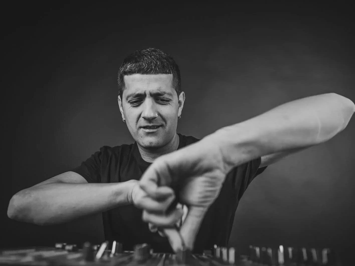 Pablo Picón manipulando la mesa de mezclas con gesto enérgico en retrato en blanco y negro del DJ y speaker de ScannerFM