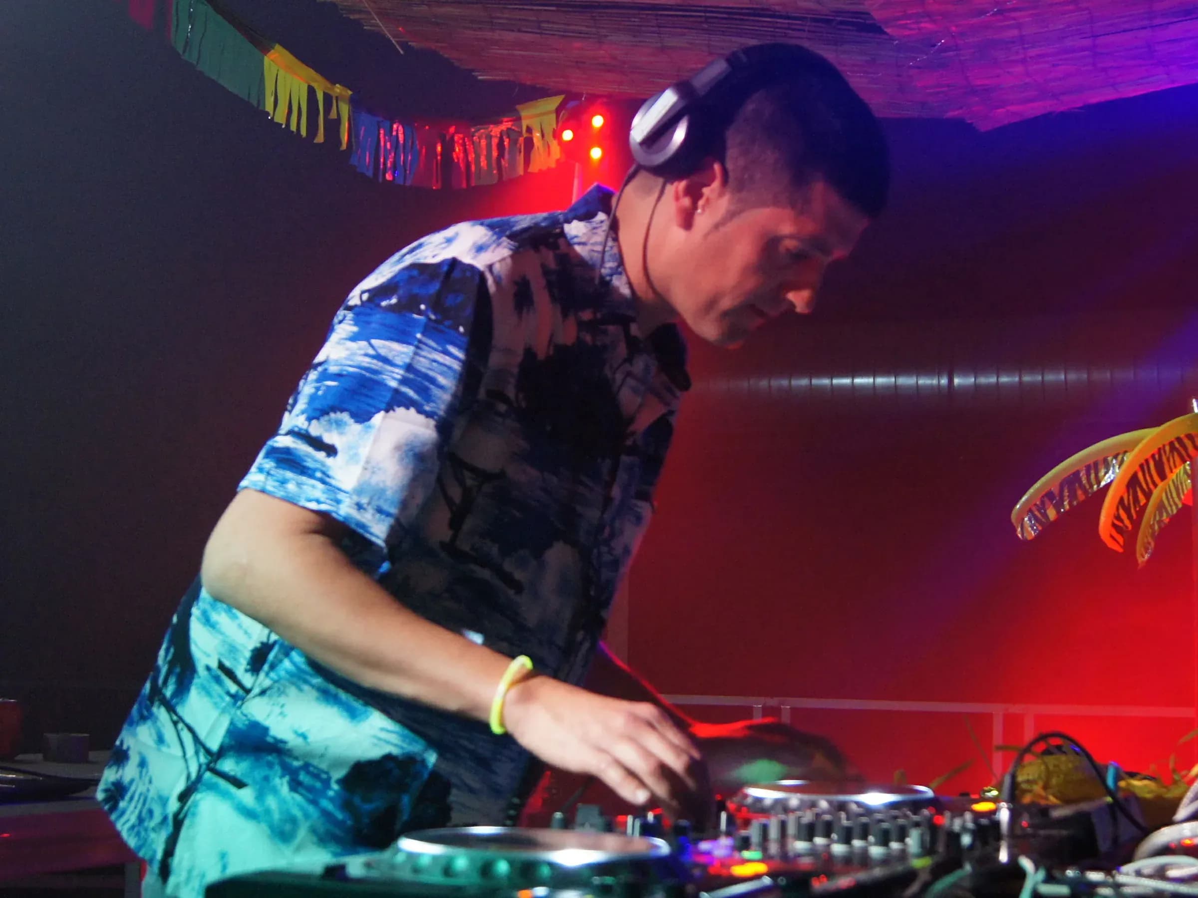 DJ Pablo con camisa hawaiana y auriculares pinchando concentrado bajo luces rojas y azules