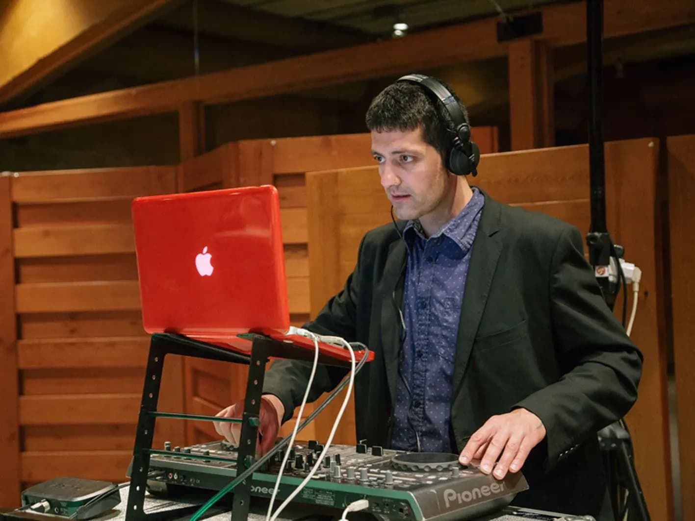 DJ Pablo con auriculares y traje oscuro manejando portatil Apple rojo y controladora Pioneer en evento