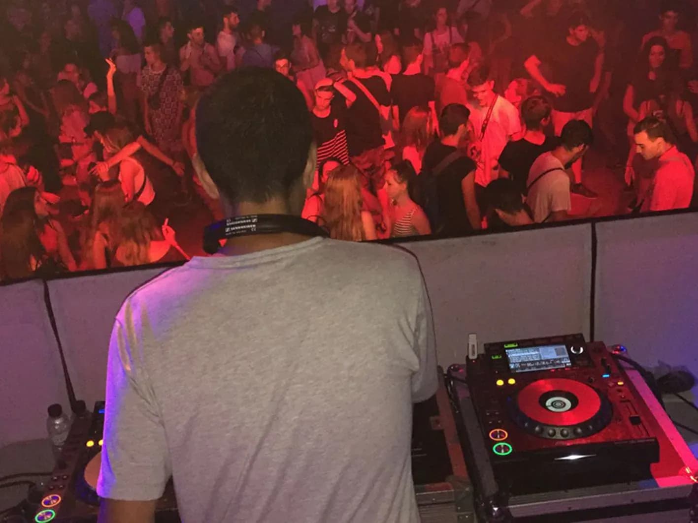 DJ Pablo de espaldas pinchando con CDJ Pioneer ante pista llena bajo luces rojas y humo en discoteca