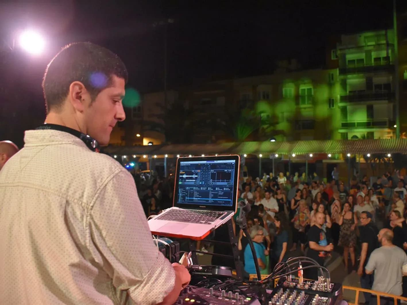 DJ Pablo de espaldas mezclando con portatil ante el publico bailando en fiesta nocturna al aire libre