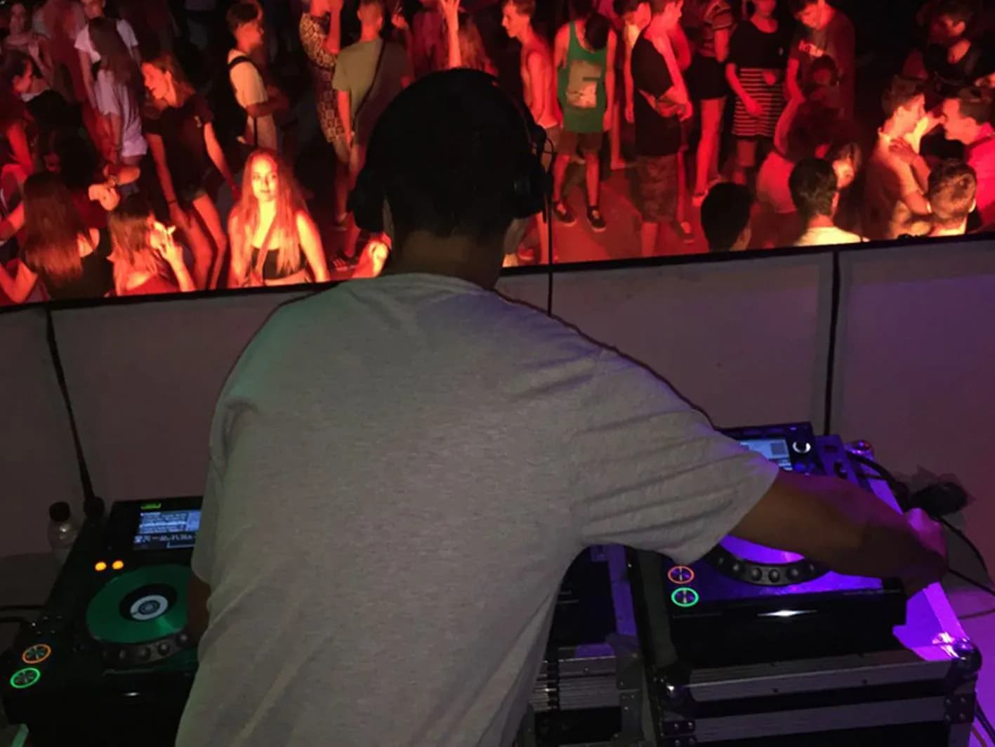 DJ Pablo de espaldas con auriculares mezclando en CDJ Pioneer frente a publico bailando bajo luces rojas
