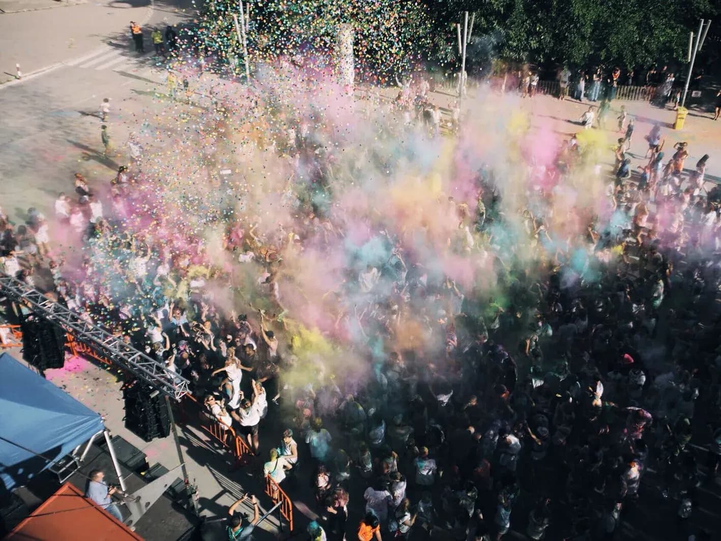Vista aerea de fiesta Holi con polvos de colores rosa, amarillo y azul sobre publico bailando en plaza al sol