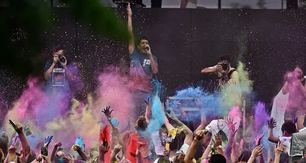 Animador subido en altura lanzando polvos rosas y azules de Fiesta Holi sobre publico con brazos levantados