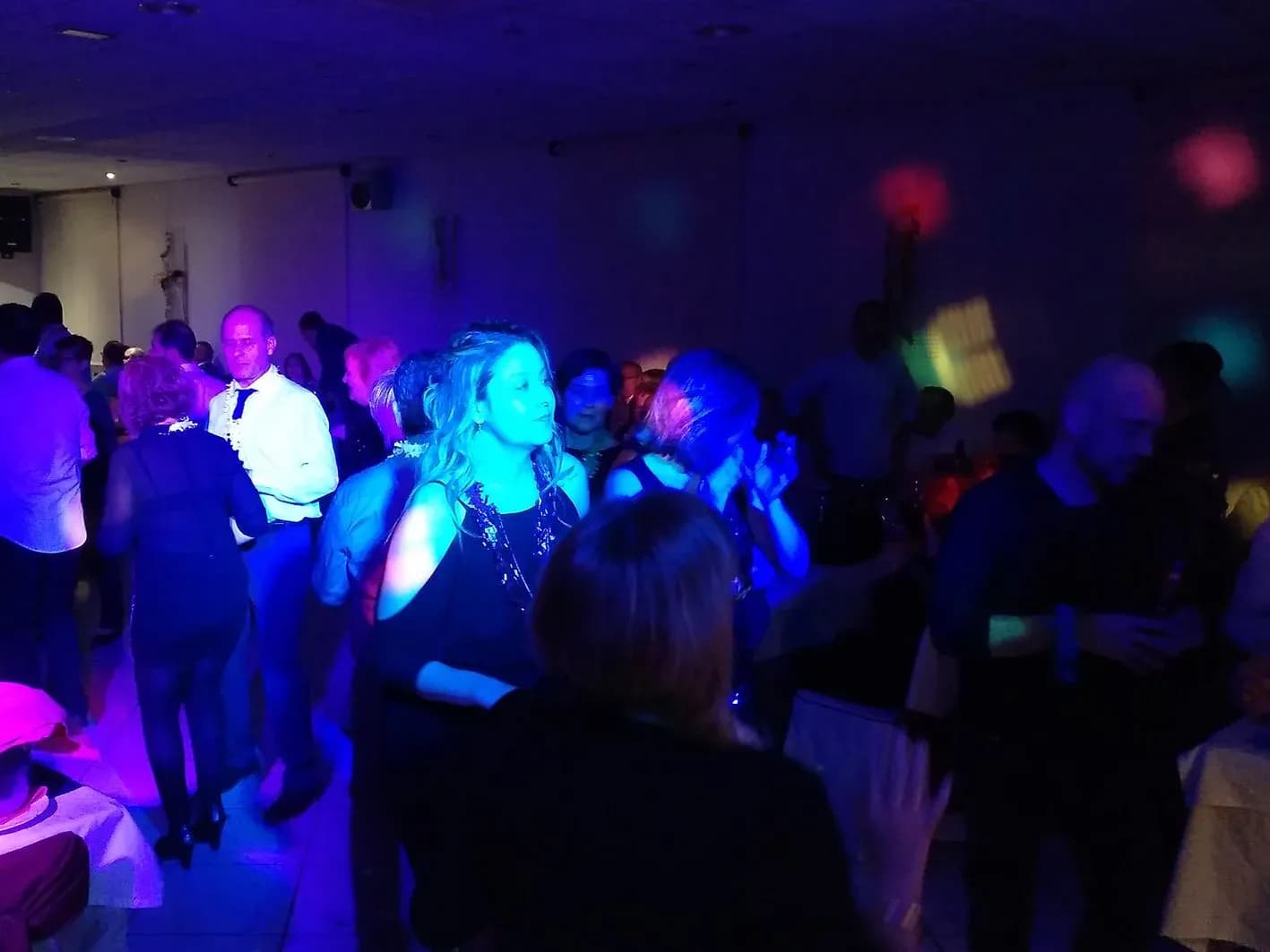 Invitados bailando en pista bajo iluminación de colores con focos circulares en fiesta de empresa nocturna en sala