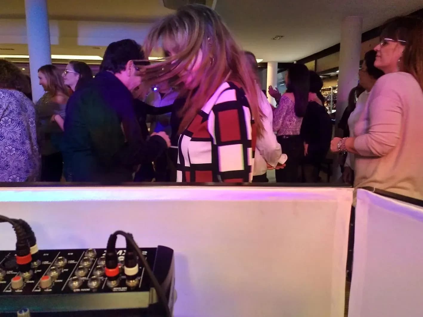 Invitados bailando junto a cabina de DJ retroiluminada con mesa de mezclas en fiesta corporativa en restaurante panorámico