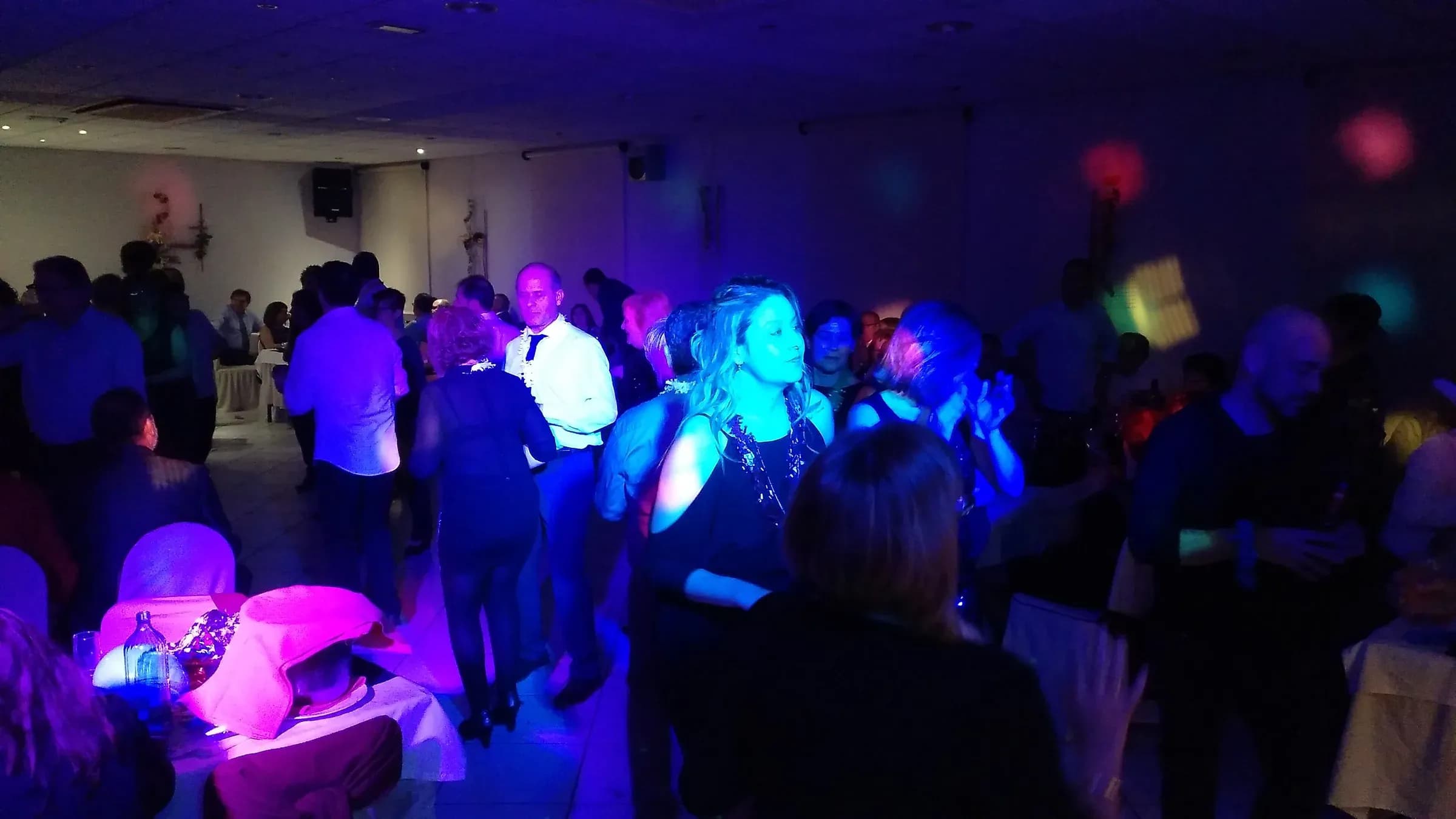 Asistentes bailando en pista de fiesta de empresa con iluminacion azul y morada de discomovil en sala interior