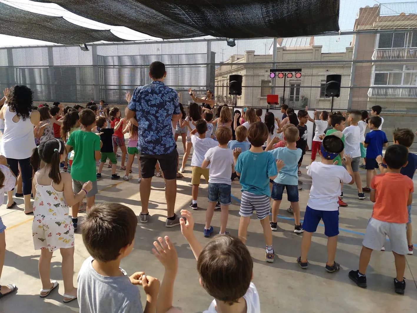 Animador con camisa estampada bailando frente a grupo numeroso de niños en patio escolar al aire libre