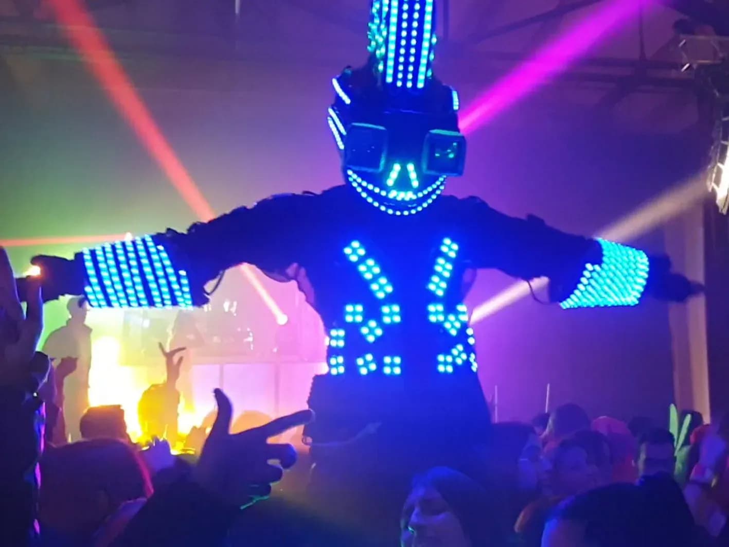 Robot LED gigante de El Fieston con traje azul iluminado y publico levantando manos bajo focos verdes y violetas