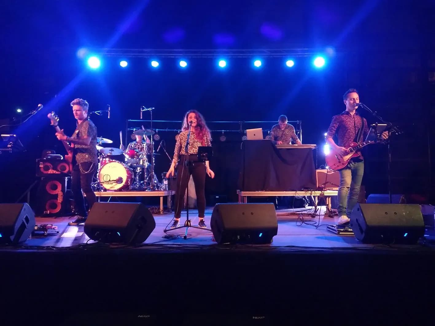 Mind Trick en directo sobre escenario con focos azules y batería: guitarra, bajo, voz y teclado en concierto de versiones