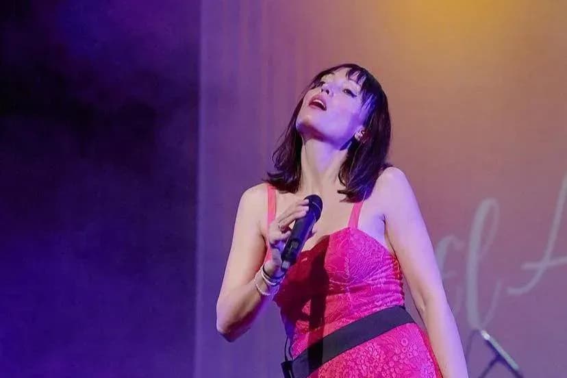 Míriam Hernández cantando con vestido rojo de encaje, tributo en femenino a Alejandro Sanz bajo luz cálida del escenario
