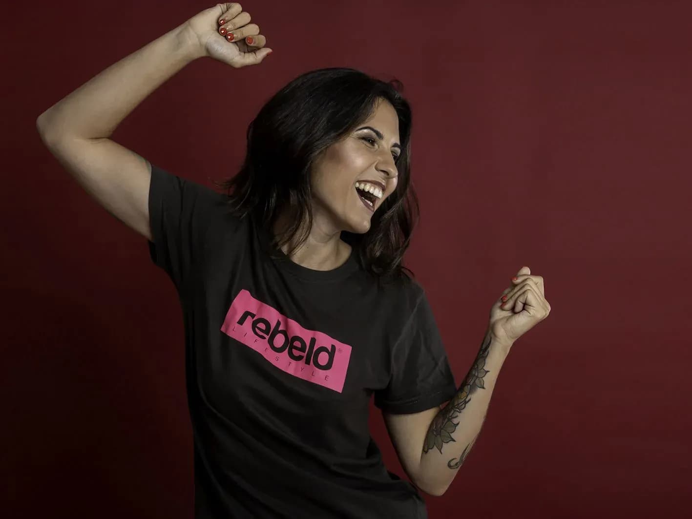 Nuria Scarp riendo y bailando con camiseta Rebeld sobre fondo rojo en sesion de estudio