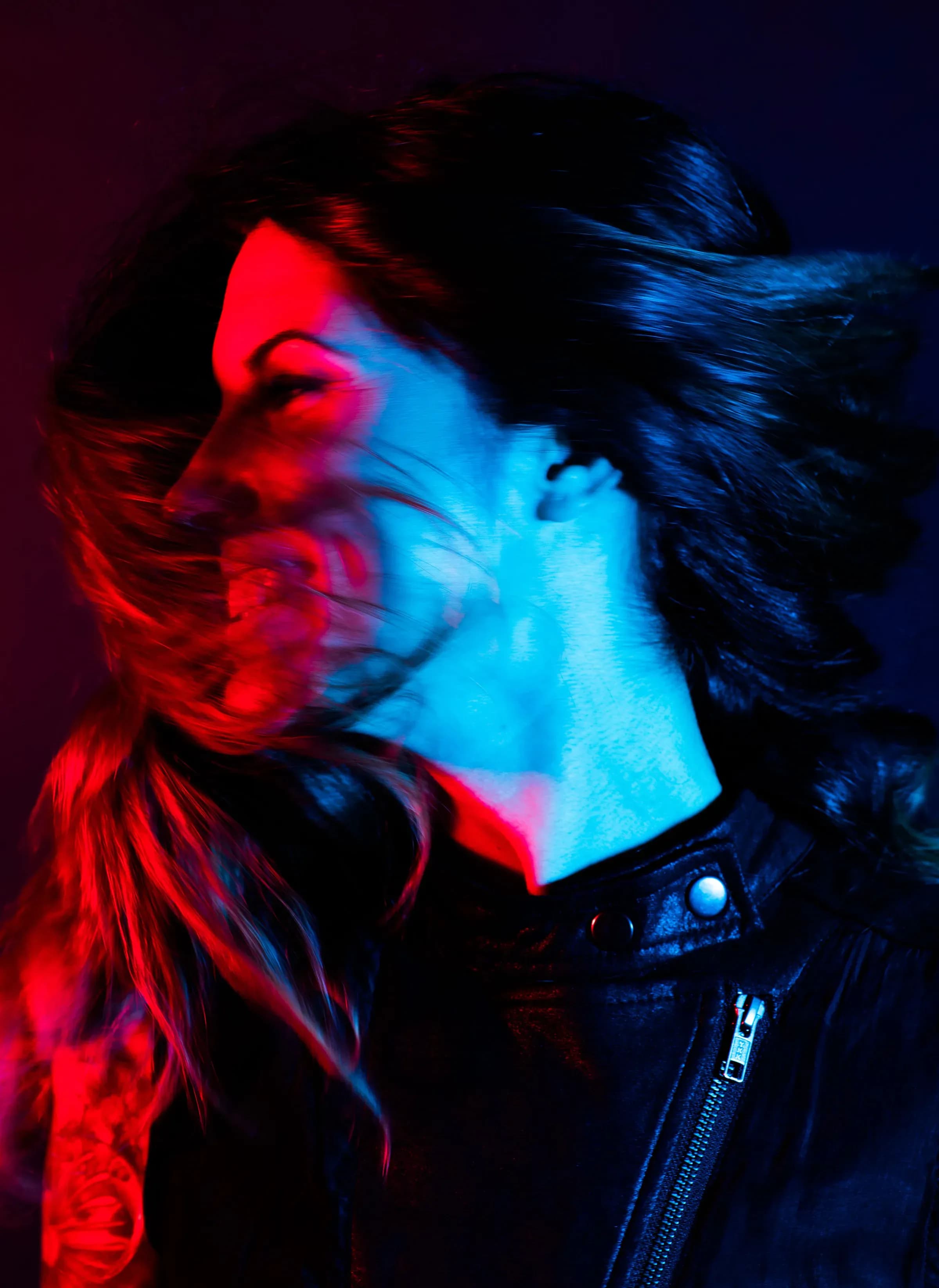 Retrato de Nuria Scarp con cazadora de cuero bajo dos luces de color rojo y azul, sesión promocional de DJ techno