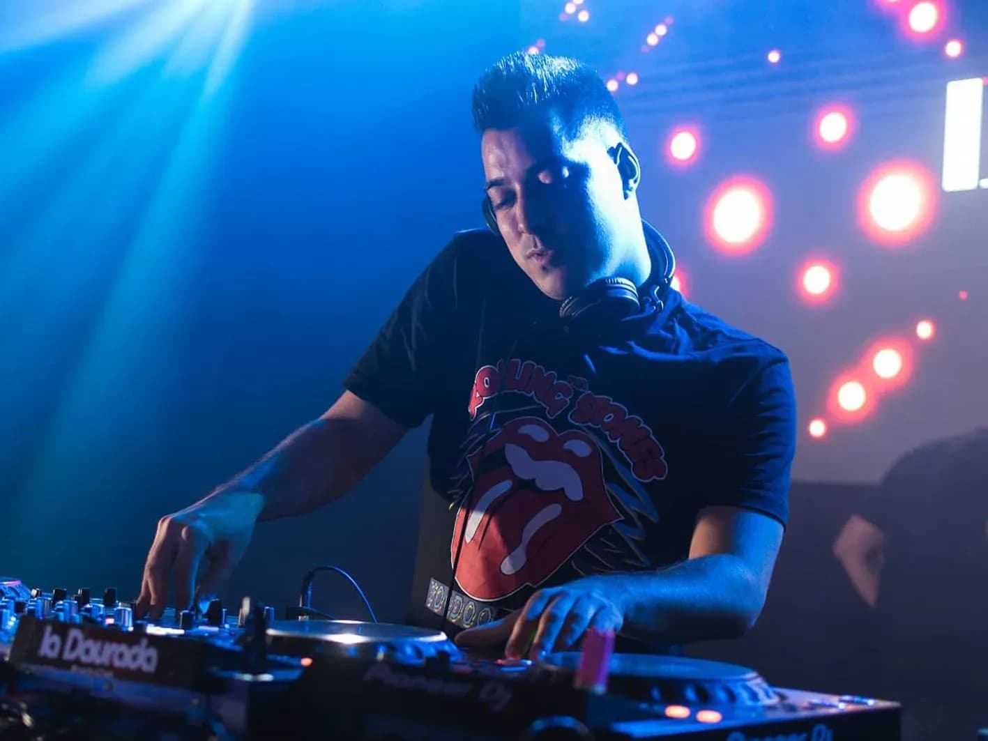Quim Martínez con camiseta de los Rolling Stones manipulando mesa Pioneer ante muro de bombillas rojas en sala nocturna