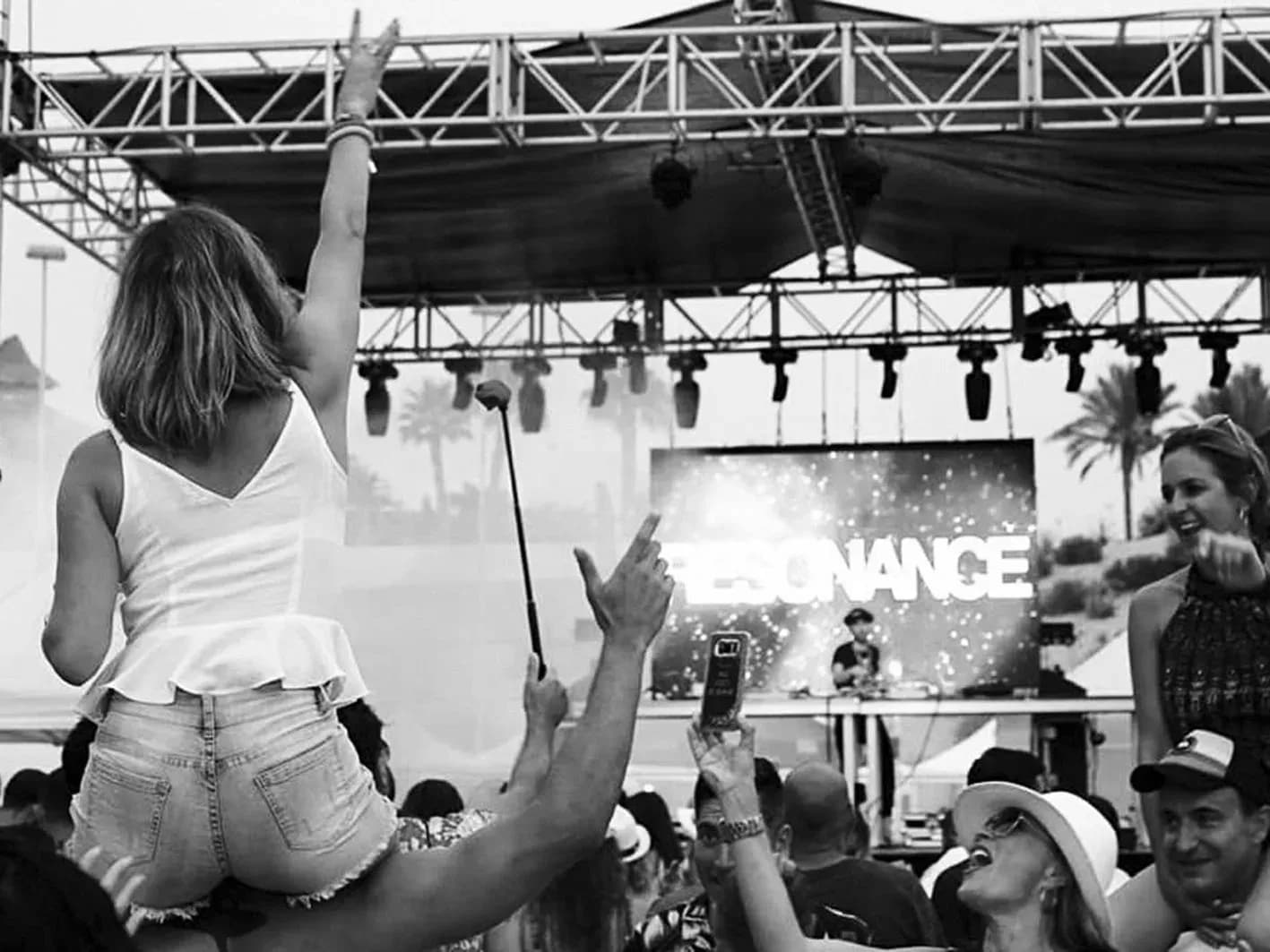 Público levantando los brazos frente al cartel Resonance en escenario al aire libre con palmeras, festival de electrónica