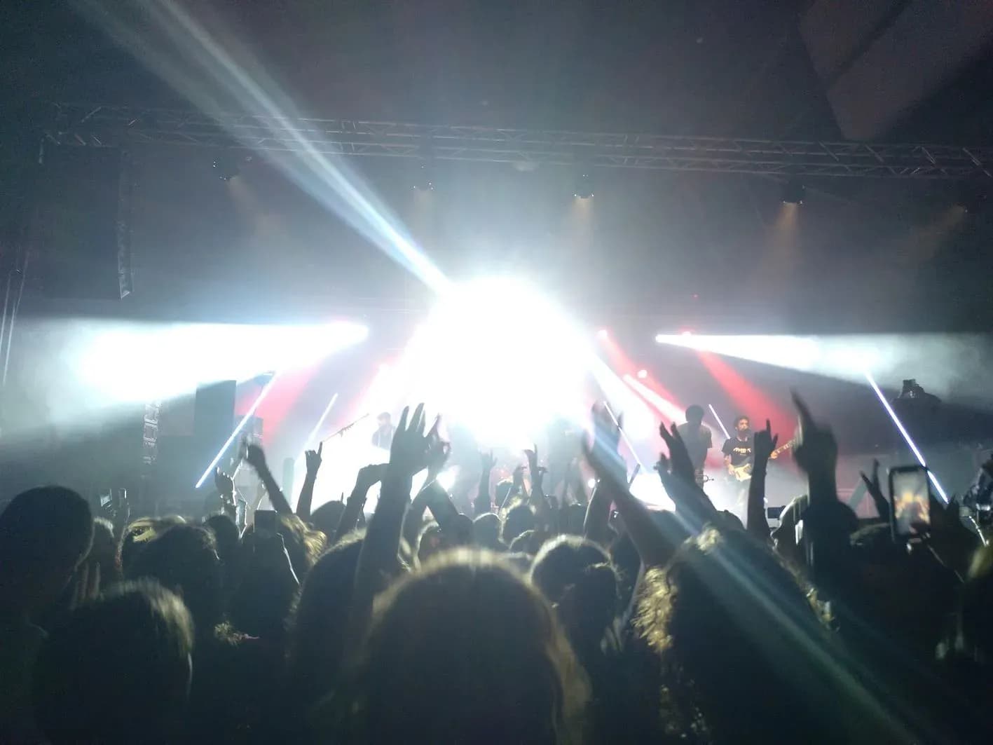 Vista del público frente al escenario iluminado con focos cruzados y rayos sobre concierto en sala grande, sonorización en directo