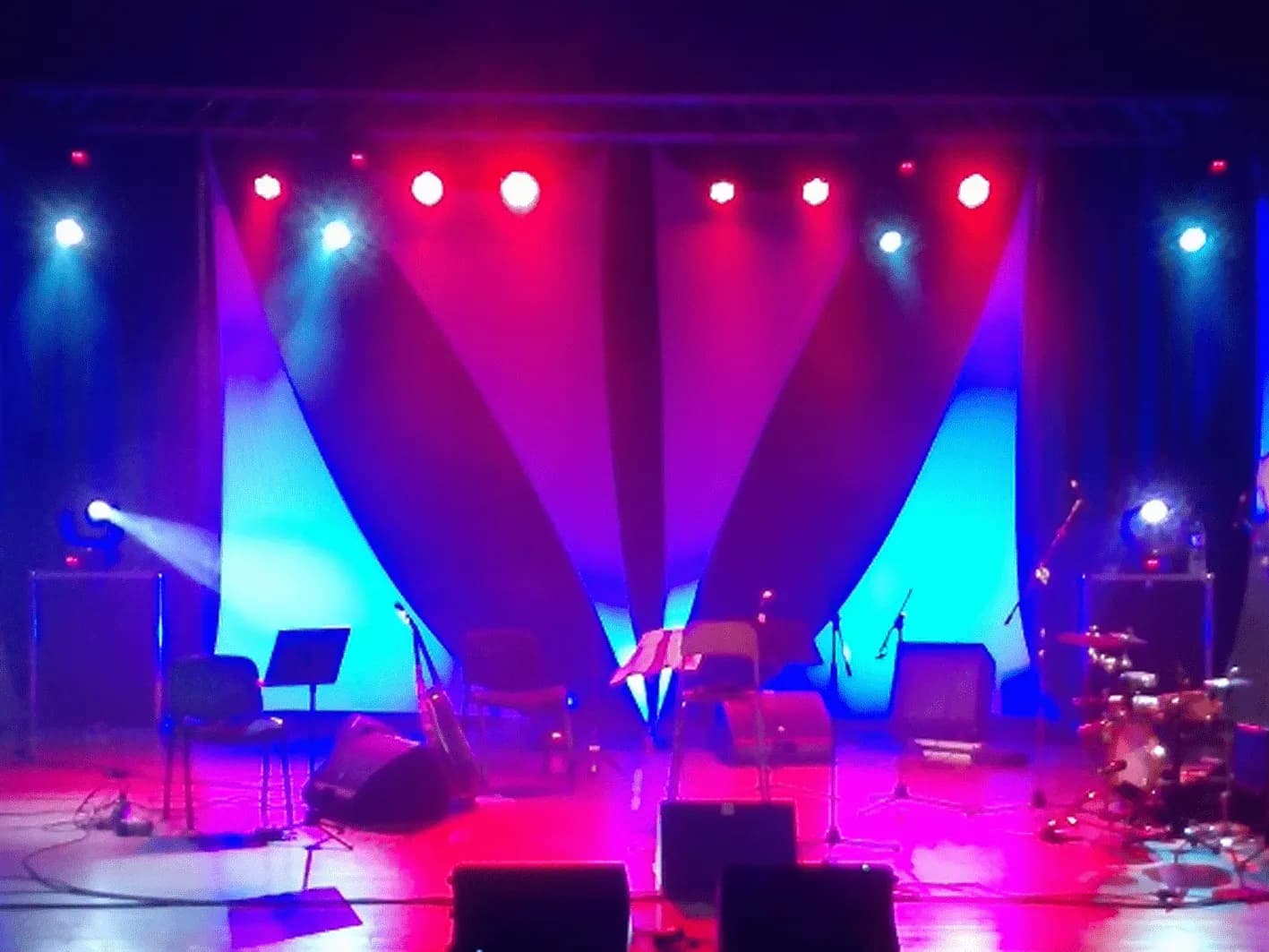Escenario de teatro con telones azules y rojos iluminados por focos cenitales rosas y rojos antes del show