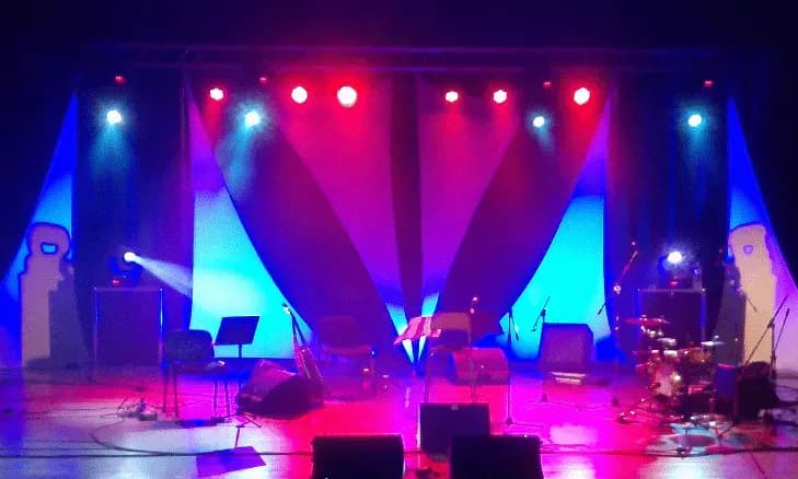Escenario vacio con telones blancos iluminado en azul y rojo con focos PAR y bateria preparada para concierto
