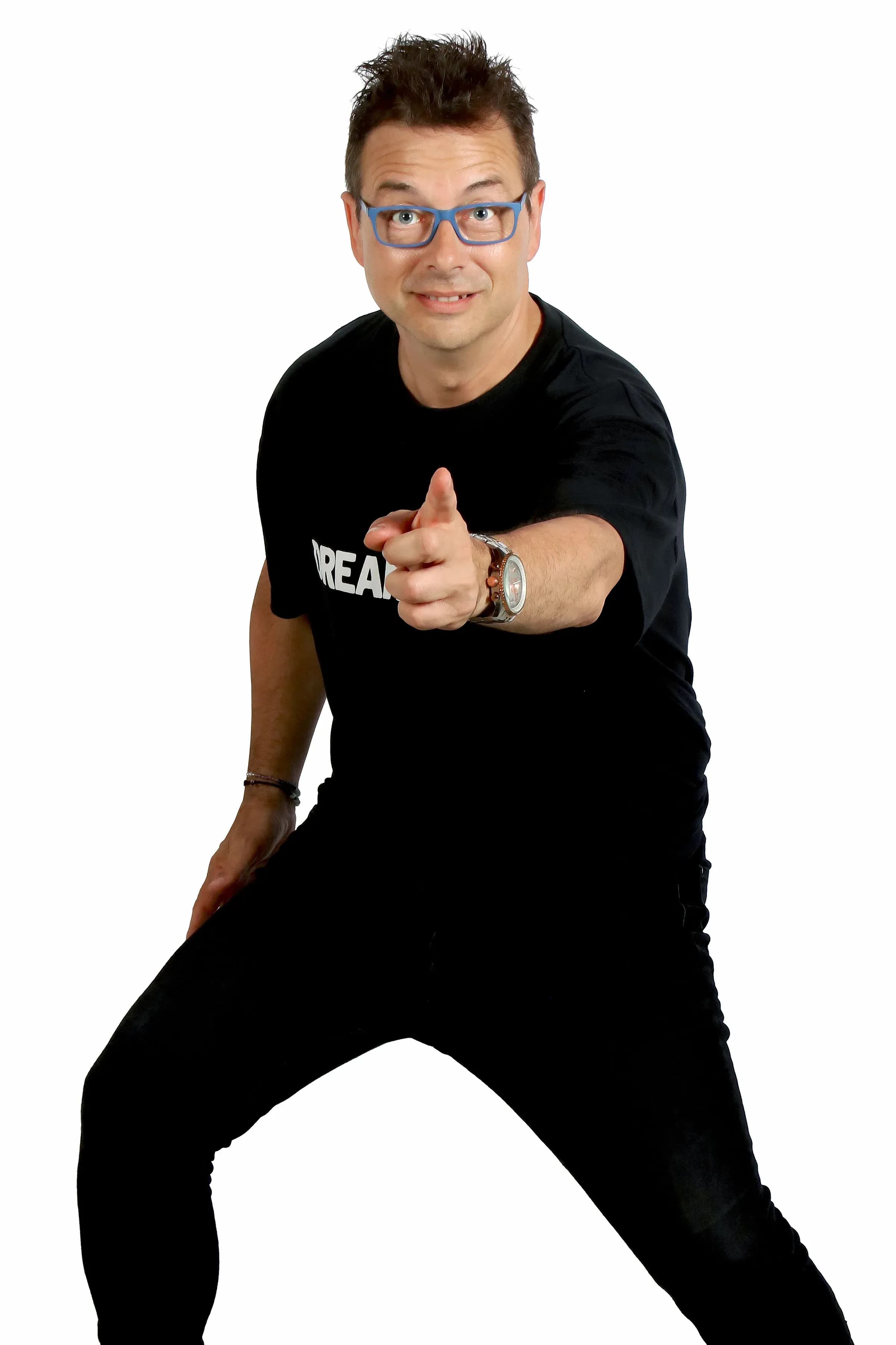 Toni Peret con gafas azules, camiseta Dream y reloj plateado señalando con el dedo a cámara sobre fondo blanco