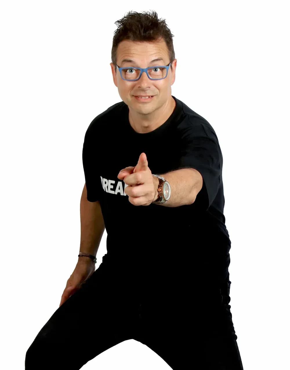 Toni Peret con gafas azules y camiseta negra senalando a camara en pose energica sobre fondo blanco