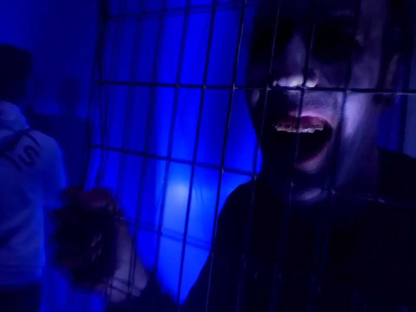 Actor maquillado tras una jaula de barrotes iluminada de azul mostrando los dientes con expresión amenazante, Túnel del Terror