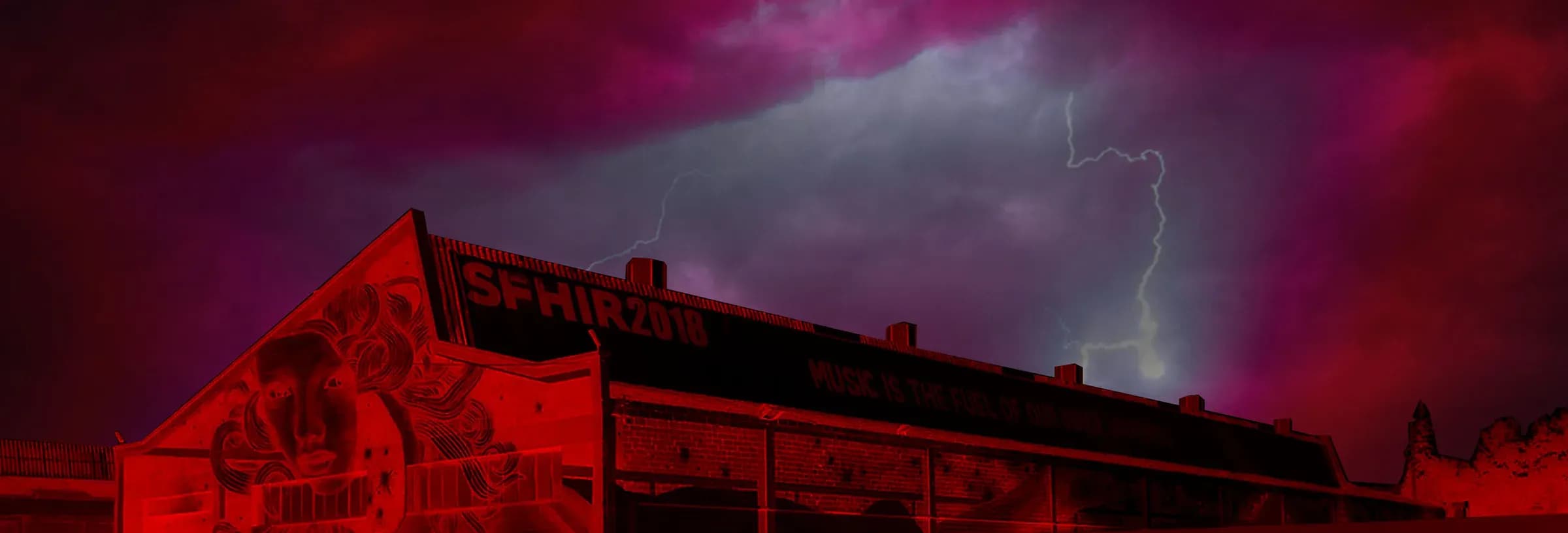 Portada del Tunel del Terror con nave industrial iluminada en rojo, mural y cielo tormentoso con rayos