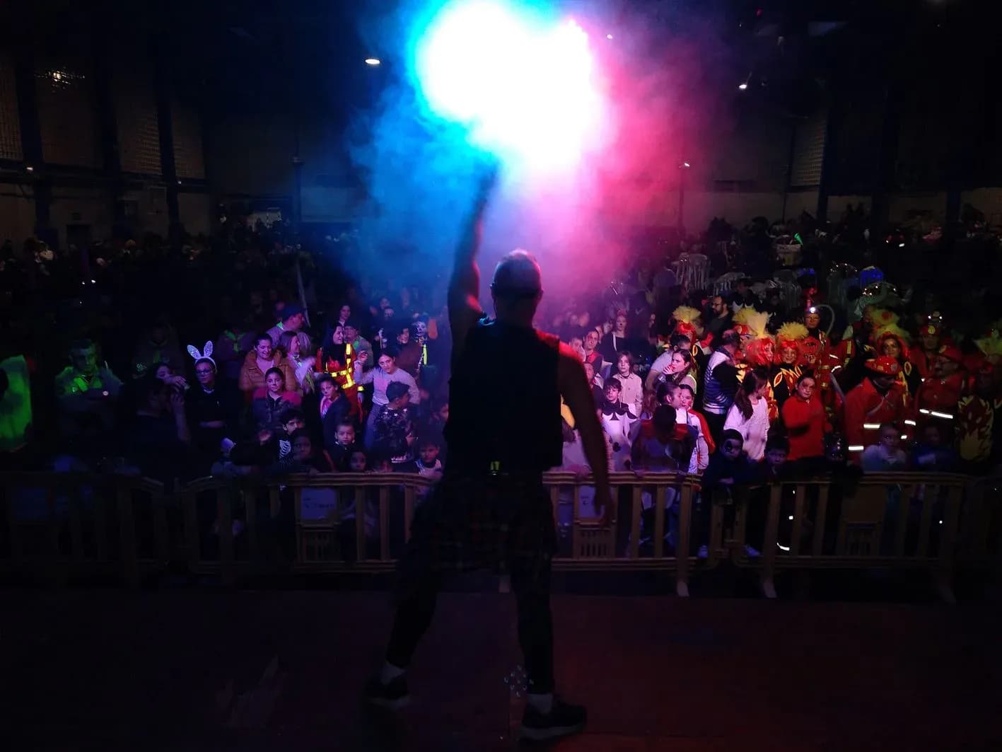 Animadores bailando coreografía sobre escenario con público al fondo en plaza decorada con guirnaldas de fiesta de pueblo