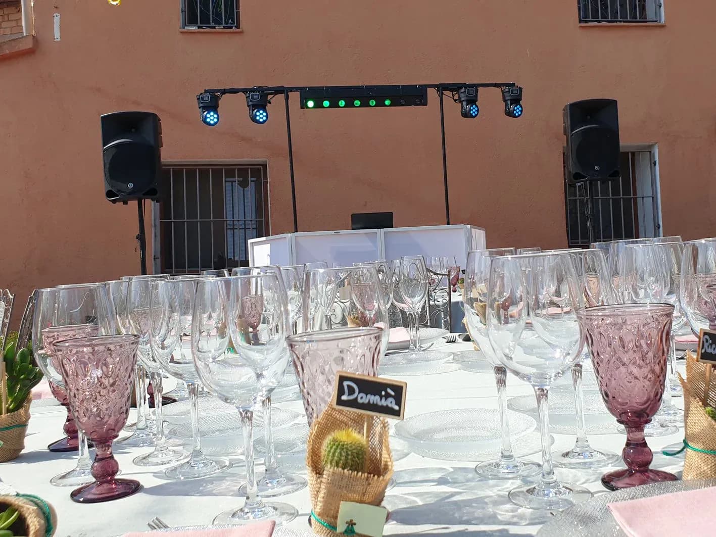 Mesa de banquete de boda con copas de cristal y altavoces al fondo, montaje de sonorización para ceremonia al aire libre