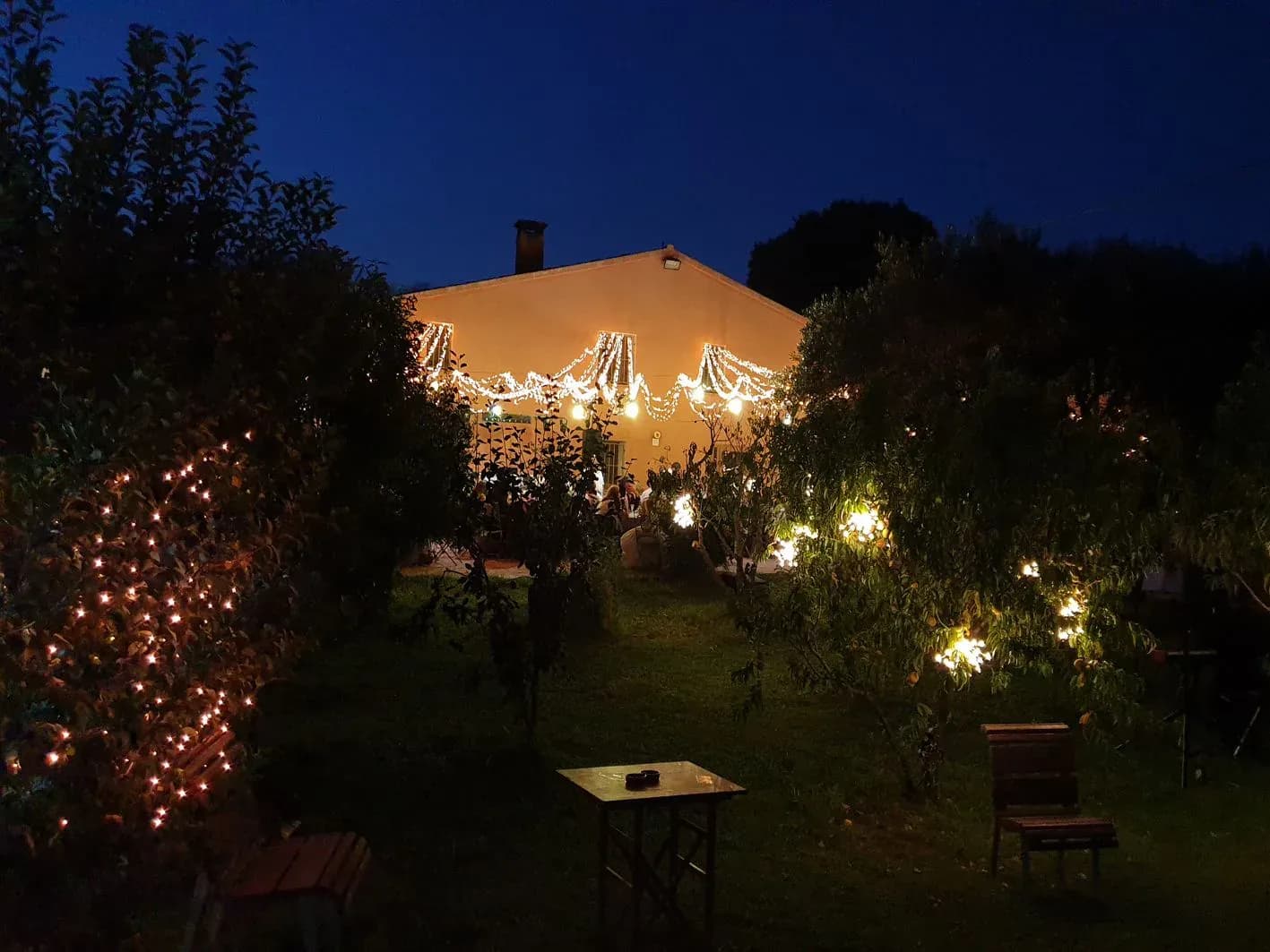 Masía iluminada con guirnaldas de luces cálidas en jardín nocturno de boda, ambientación lumínica para celebración rural