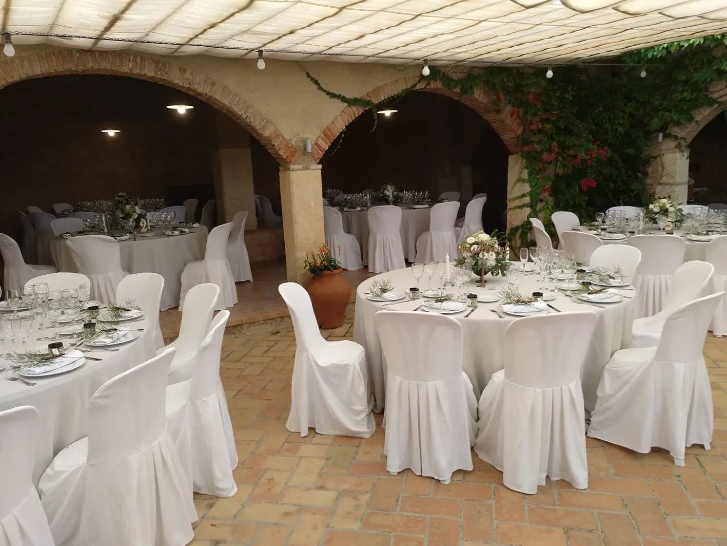 Banquete de boda montado bajo arcos de piedra con mesas redondas vestidas de blanco y centros florales
