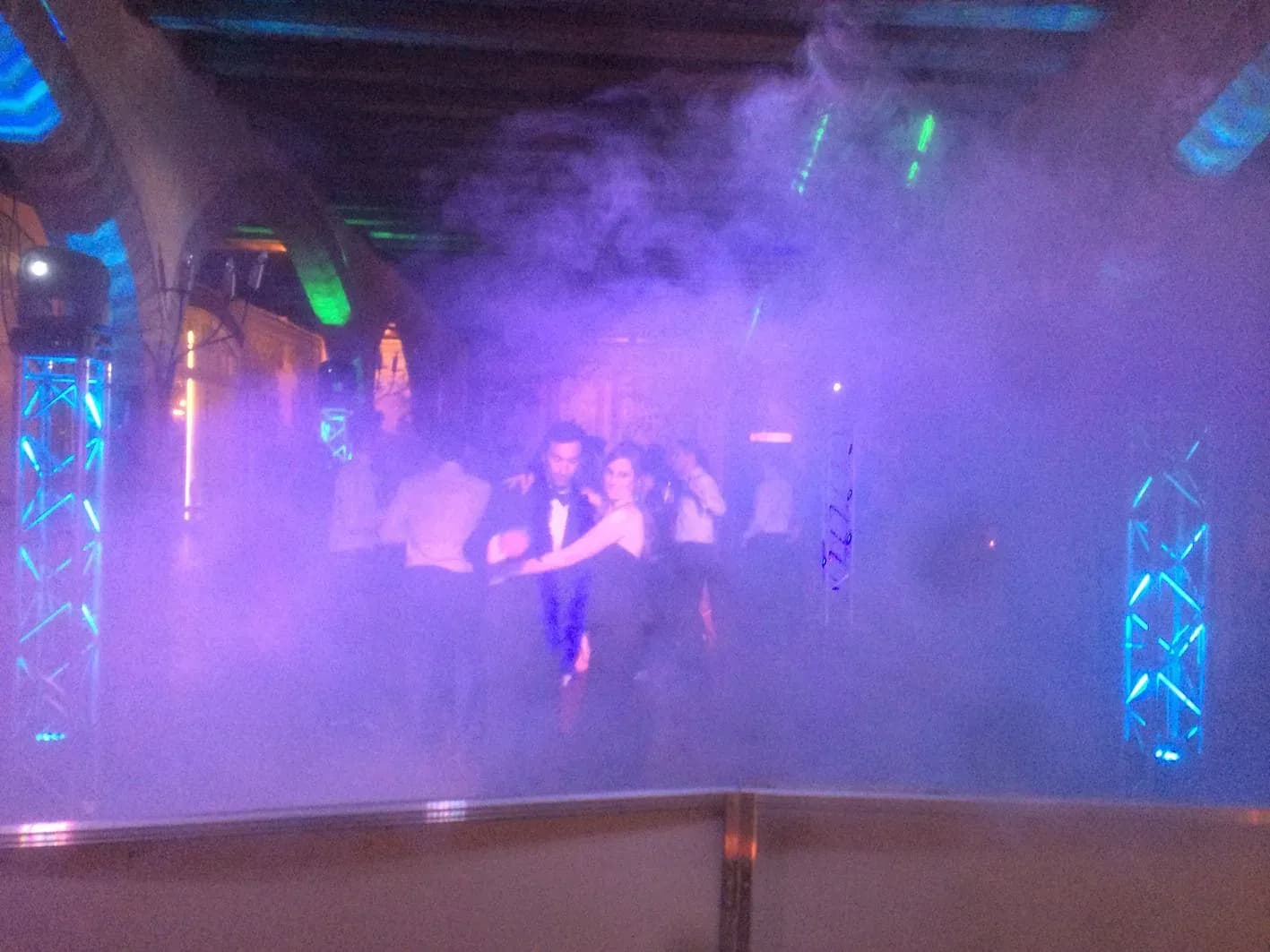 Novios bailando abrazados en pista con maquina de humo y truss iluminados de azul durante celebracion de boda nocturna