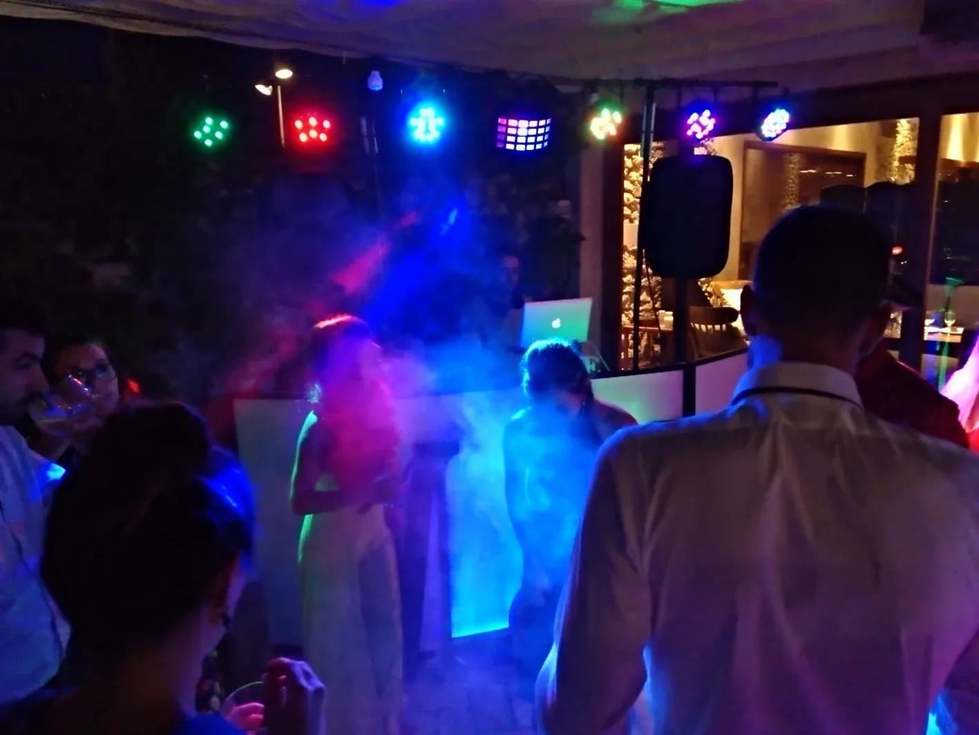 Recién casados bailando rodeados de humo y luces de colores con DJ al fondo en discomóvil de boda nocturna al aire libre