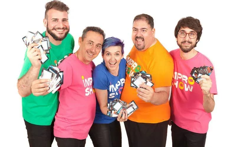 Cinco actores de Impro Show con camisetas de colores sosteniendo tarjetas de juego y sonriendo a camara