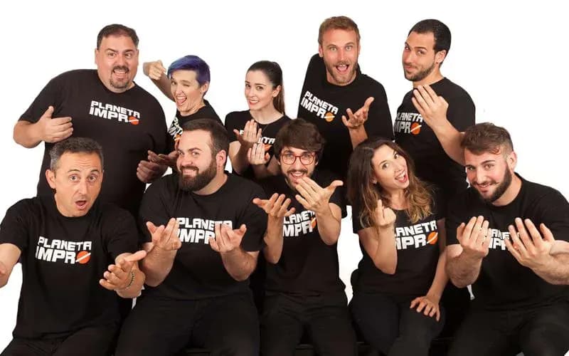 Equipo de Planeta Impro con camisetas negras gesticulando con manos abiertas en pose de grupo divertida