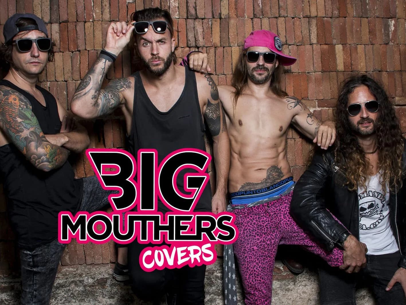 Big Mouthers Covers posando con gafas oscuras, tatuajes y pantalón fucsia ante muro de ladrillo, identidad de la banda